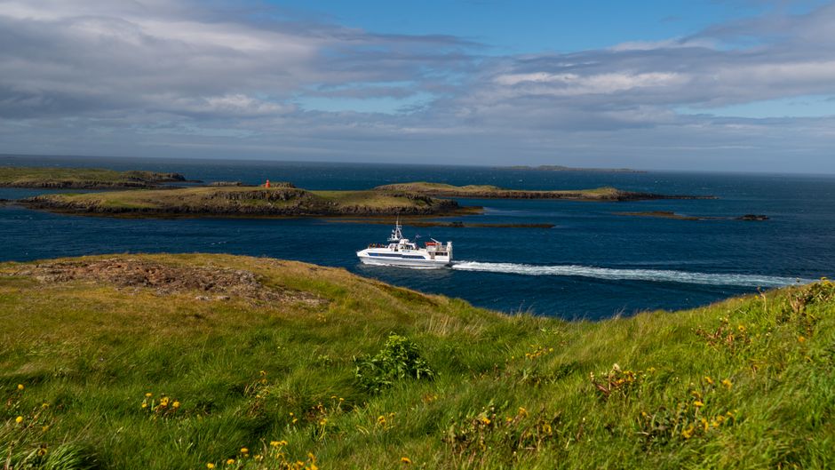 A ferry passes through picturesque coastal islands under a bright blue sky, surrounded by emerald green grass. — Photo de Zak Mir sur Pexels